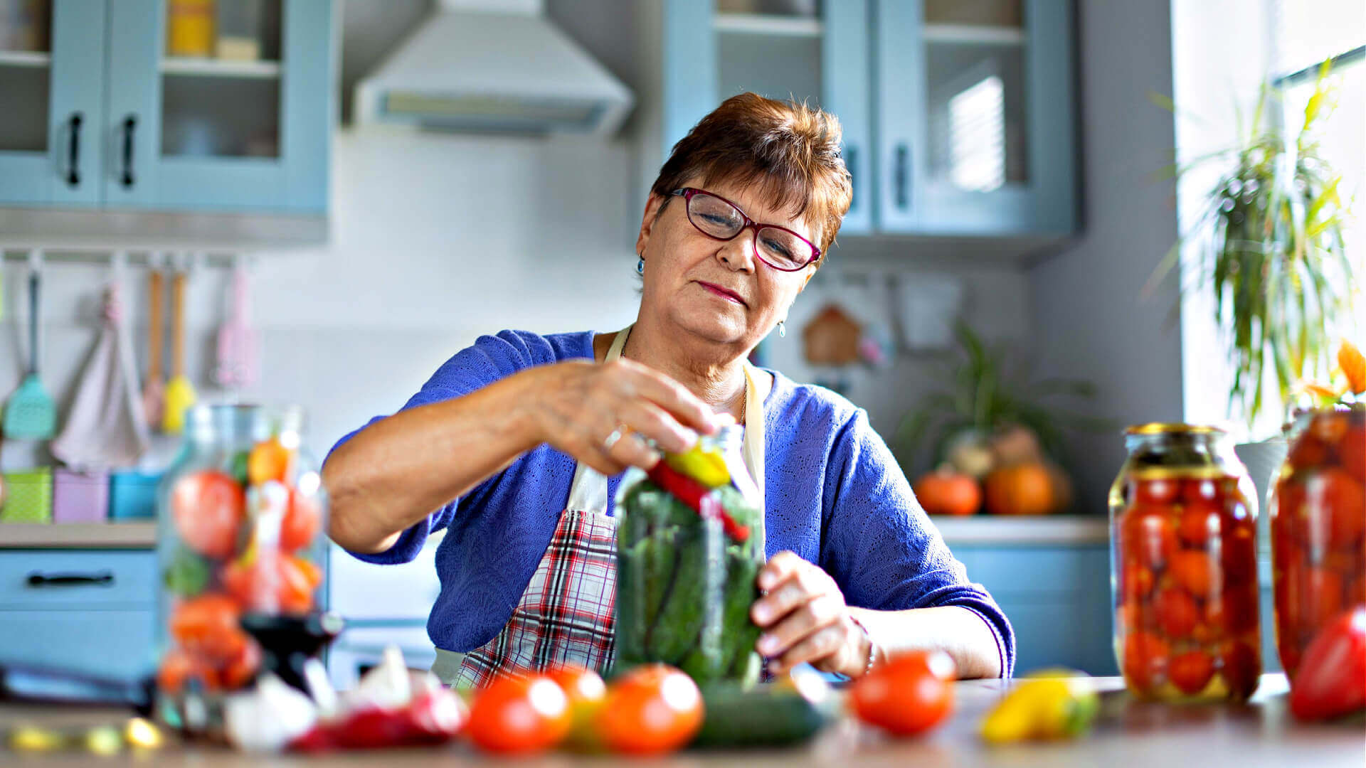 Woman preserving garden produce: peppers in jars with cucumbers