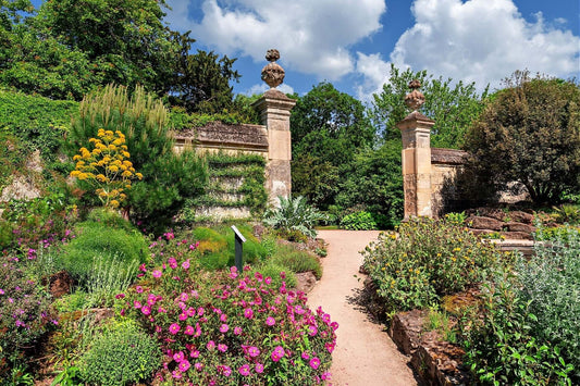 Ornate stone garden gate with finials, pink roses, lush greenery on path