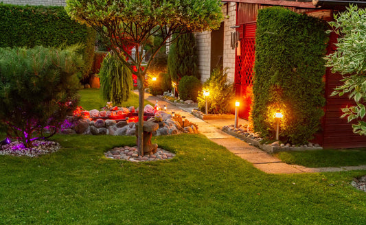 Lush green lawn with trimmed hedges, tree and warm pathway lights in night garden