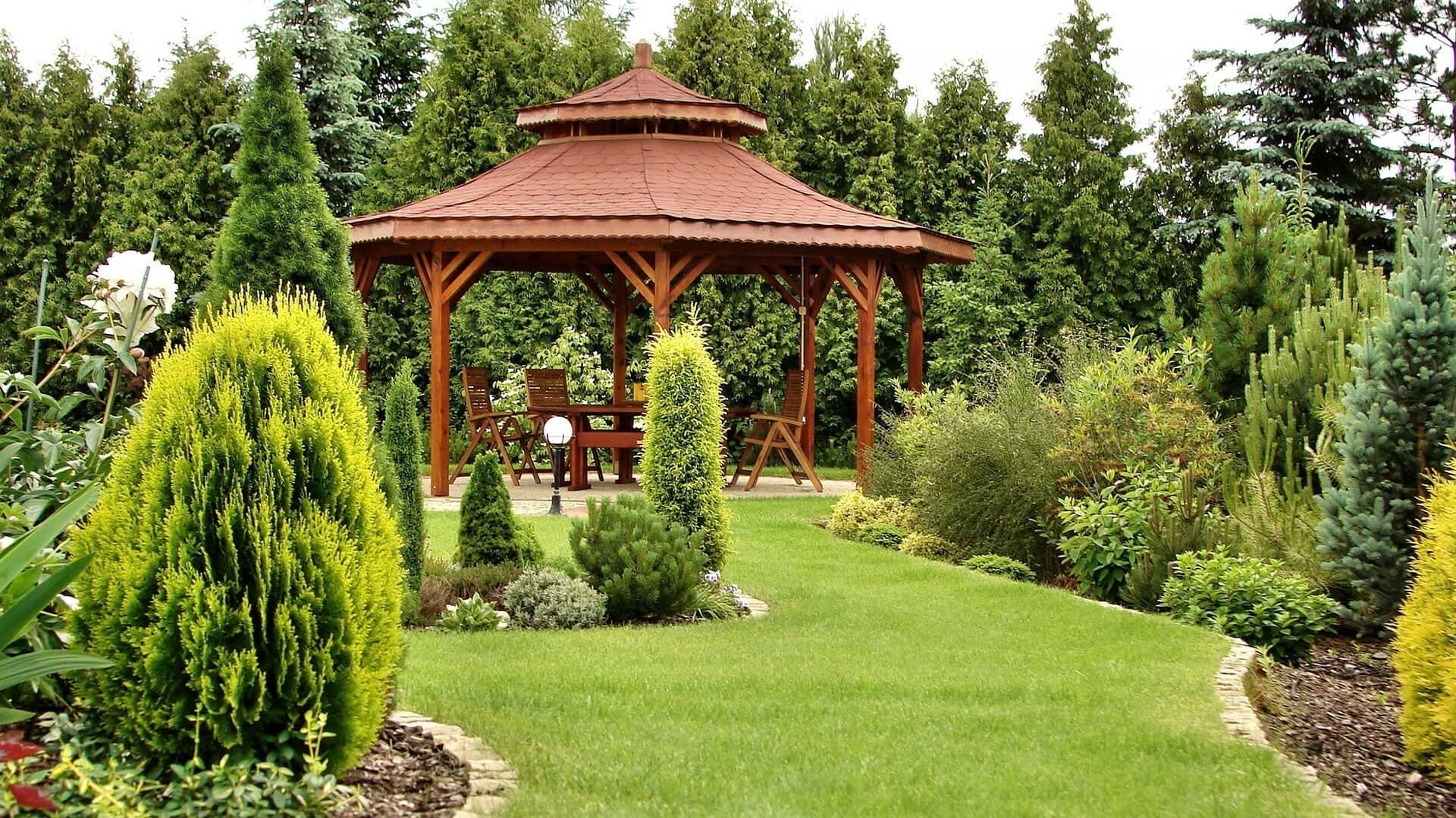Wooden gazebo with reddish-brown roof amid lush garden greenery