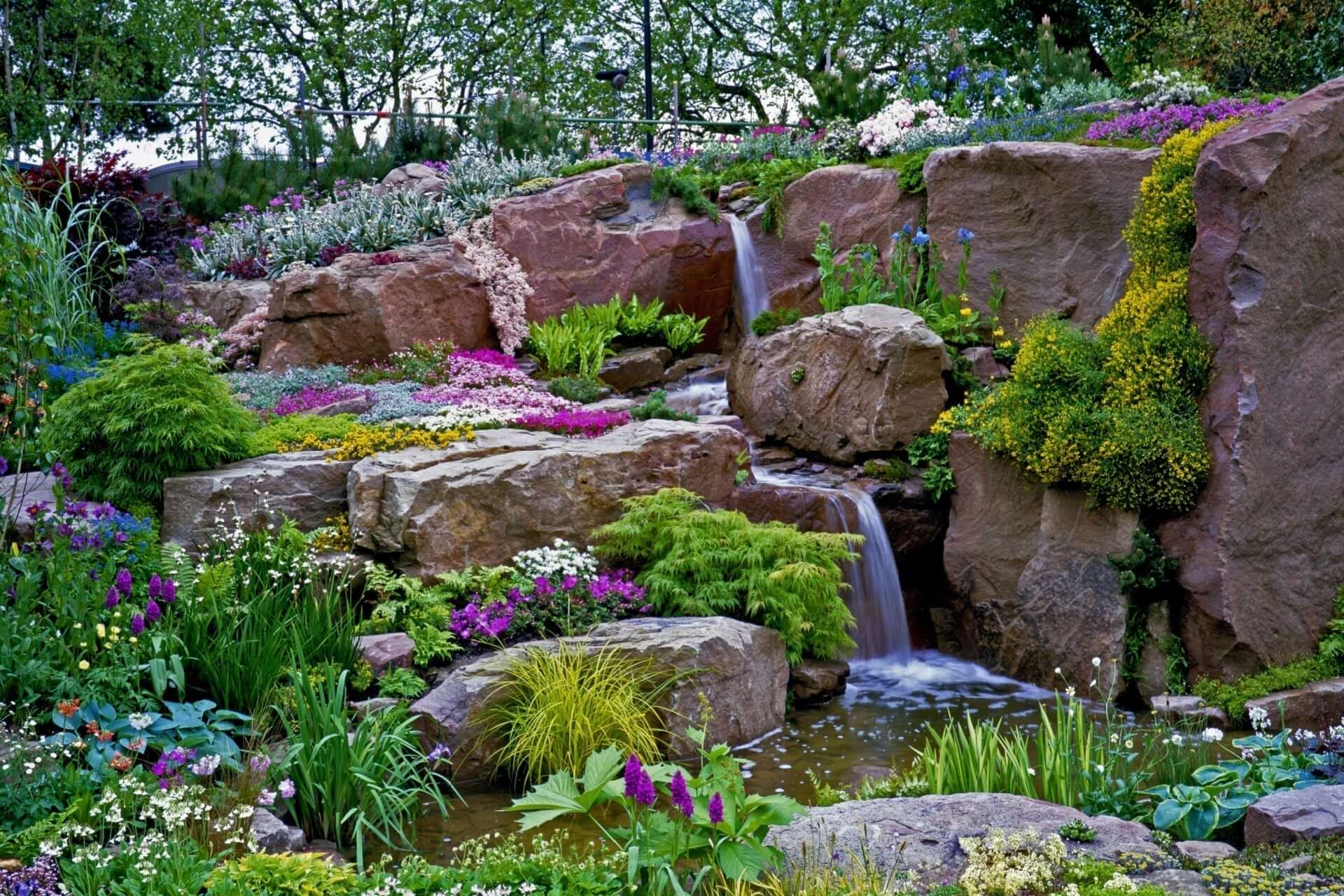 Miniature mountain garden waterfall cascades over reddish rocks into pool