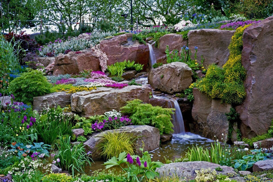 Miniature mountain garden waterfall cascades over reddish rocks into pool