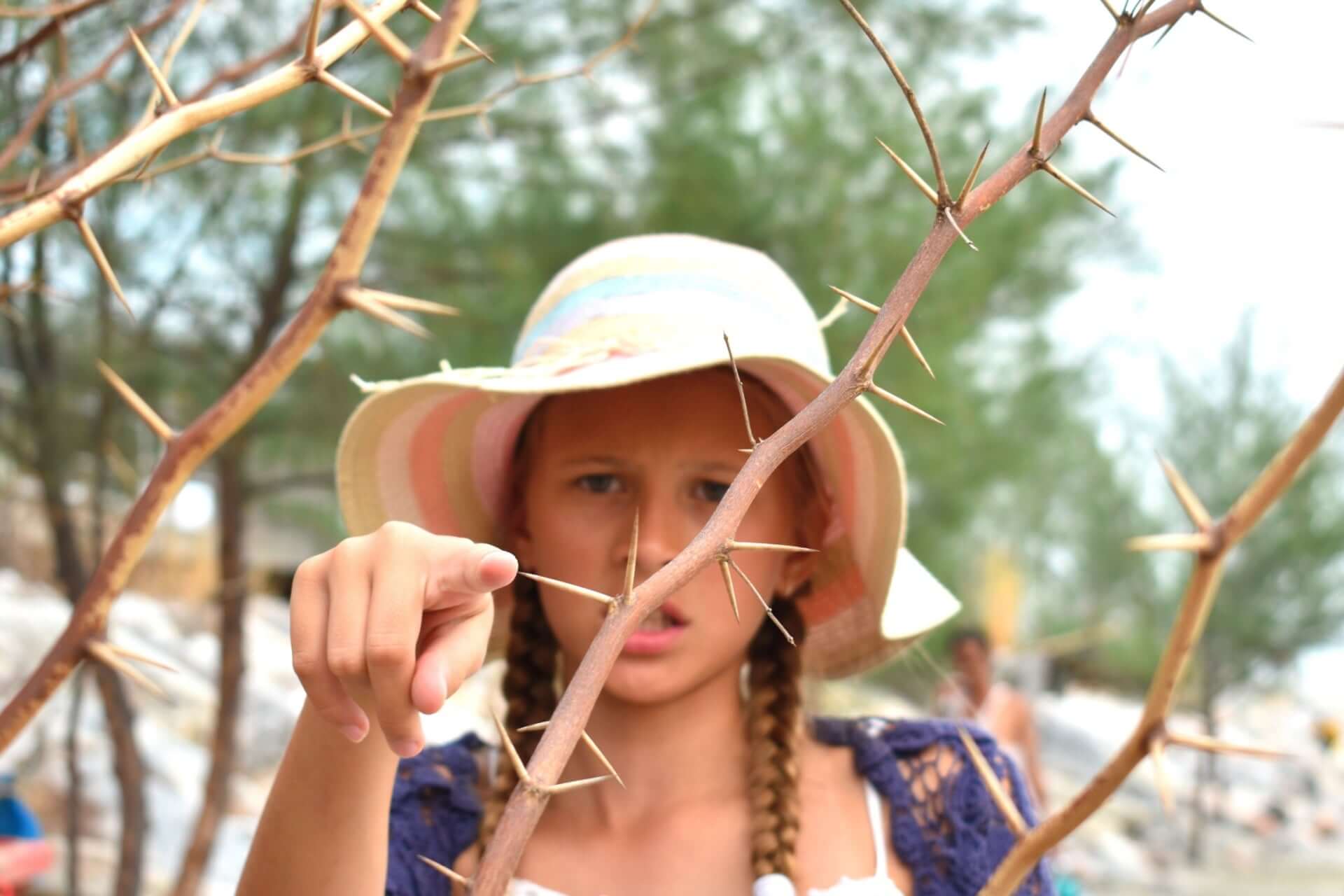 Young girl in striped hat and braids points at thorny branches