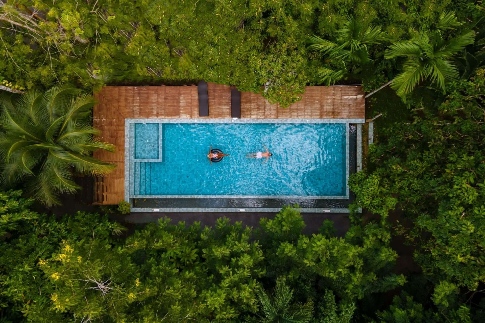 Rectangular blue pool with wooden deck and lush greenery