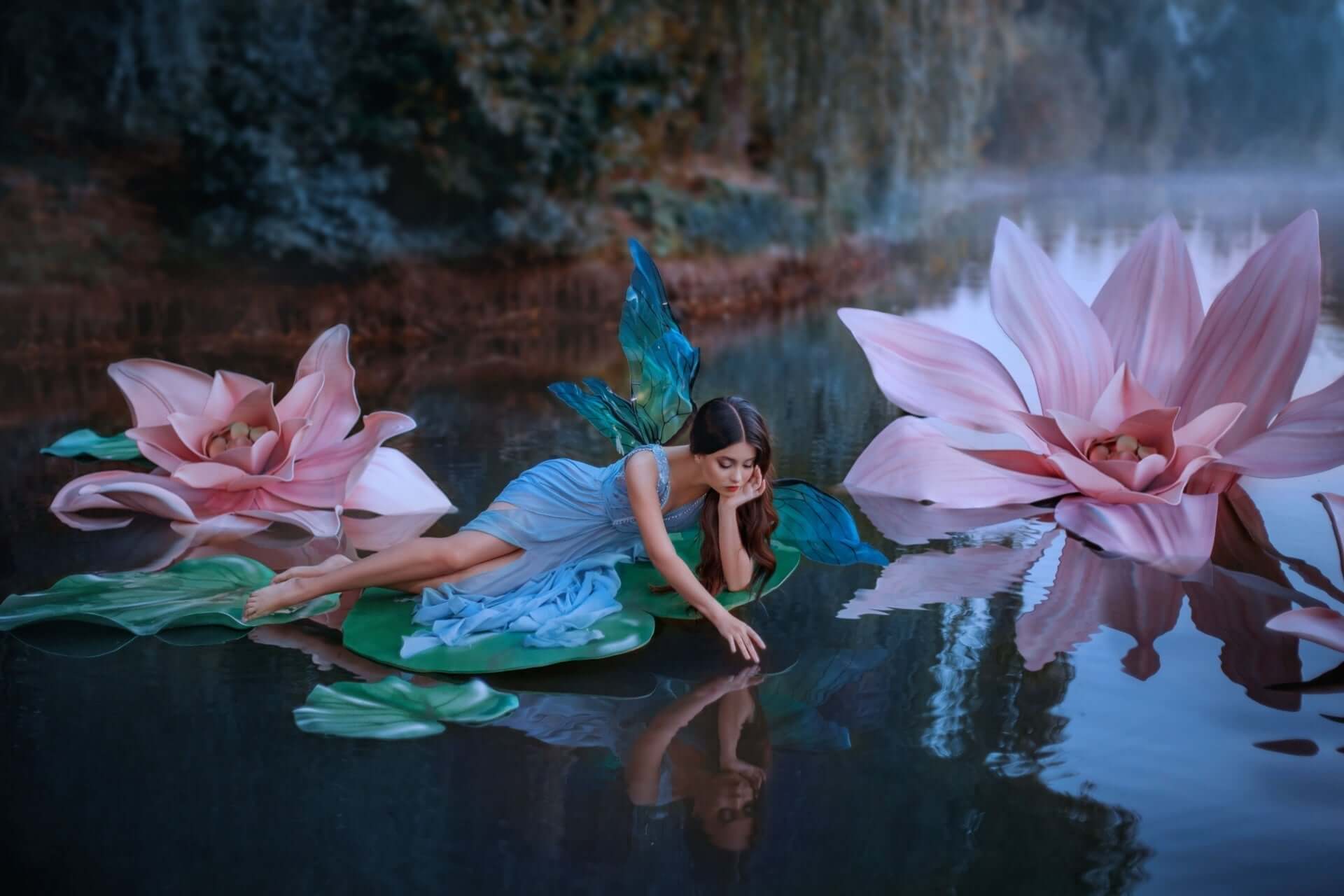 Fairy with turquoise wings on giant lily pad amid pink lotus in garden