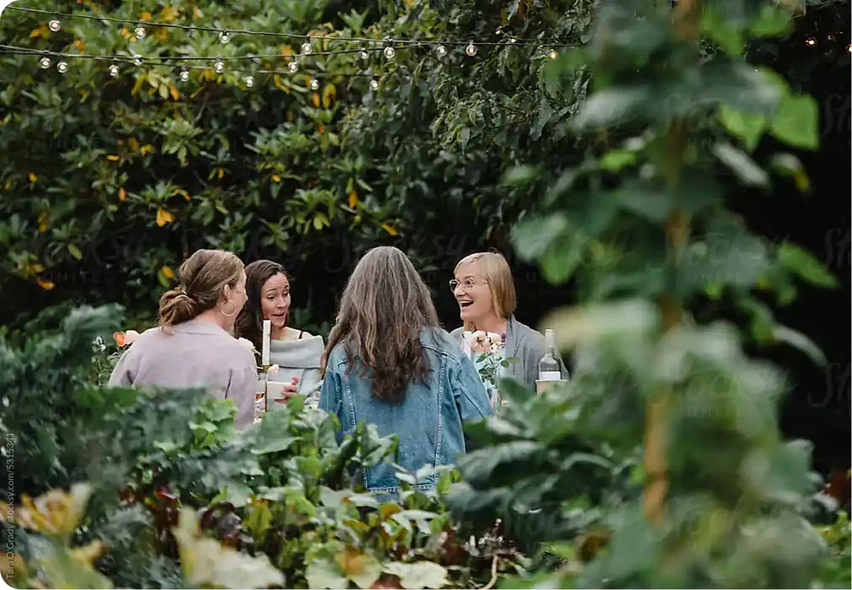 Women gardeners chatting in garden under string lights